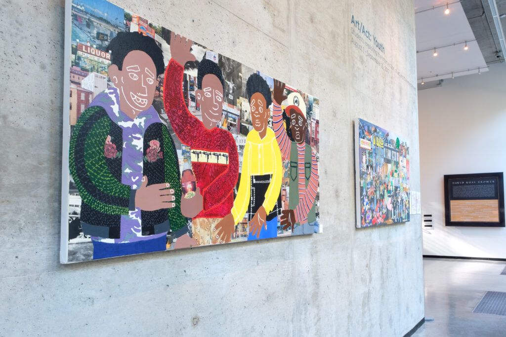 painting of black and brown youth against a cityscape on a gallery wall