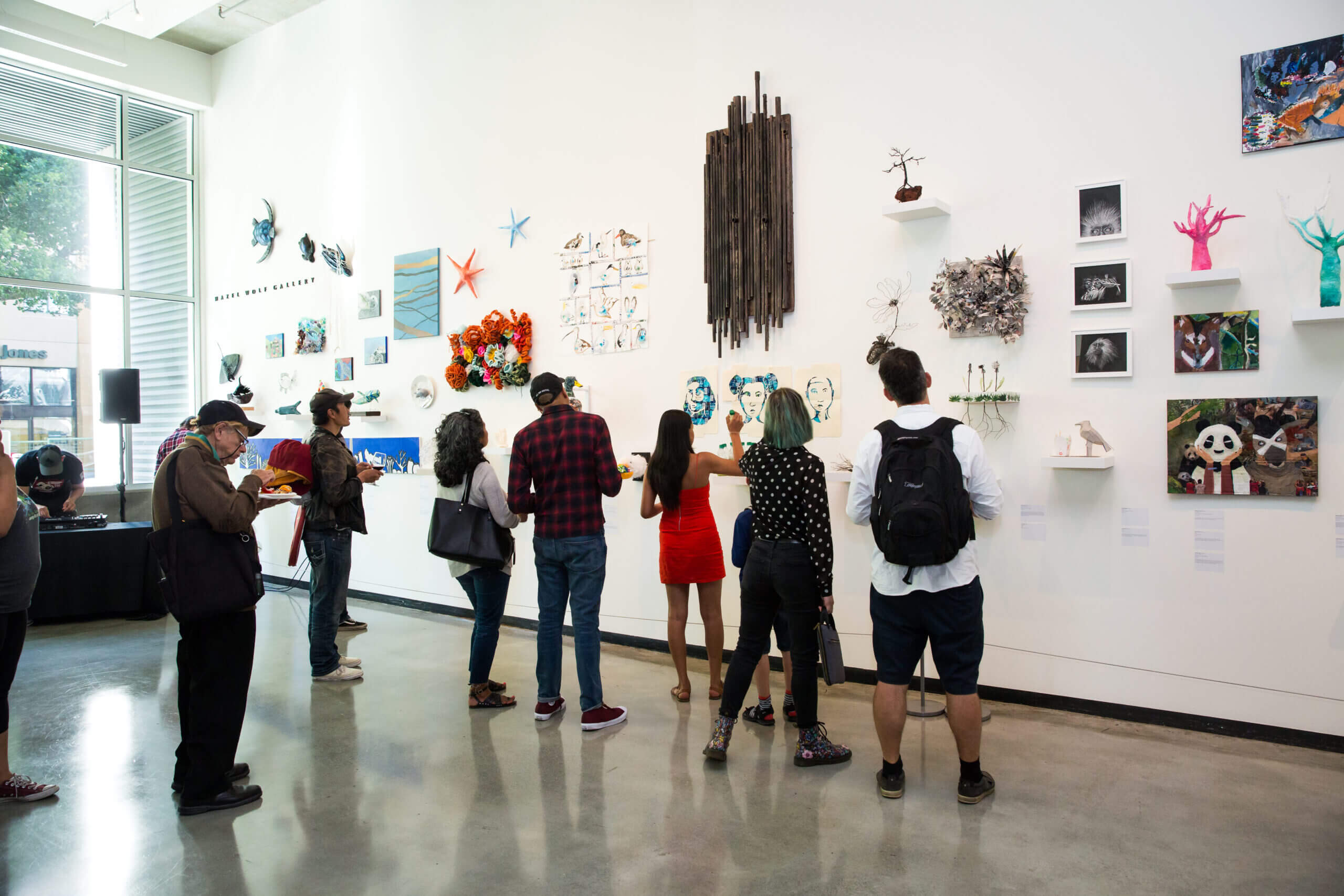 People looking at gallery wall with paintings hung, additional people in the background