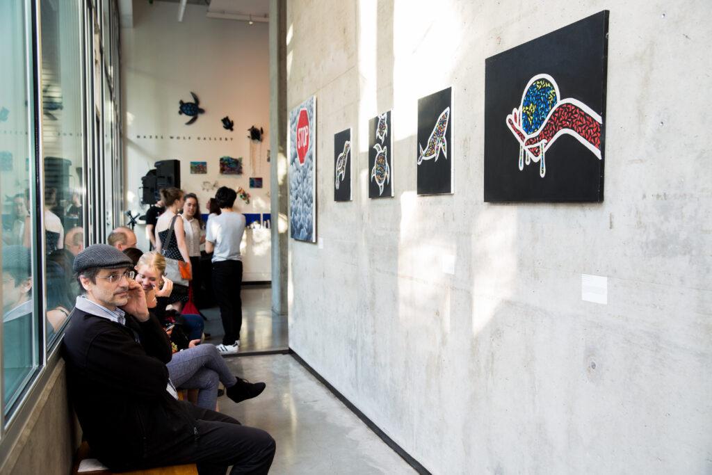 People looking at gallery wall with paintings hung, additional people in the background