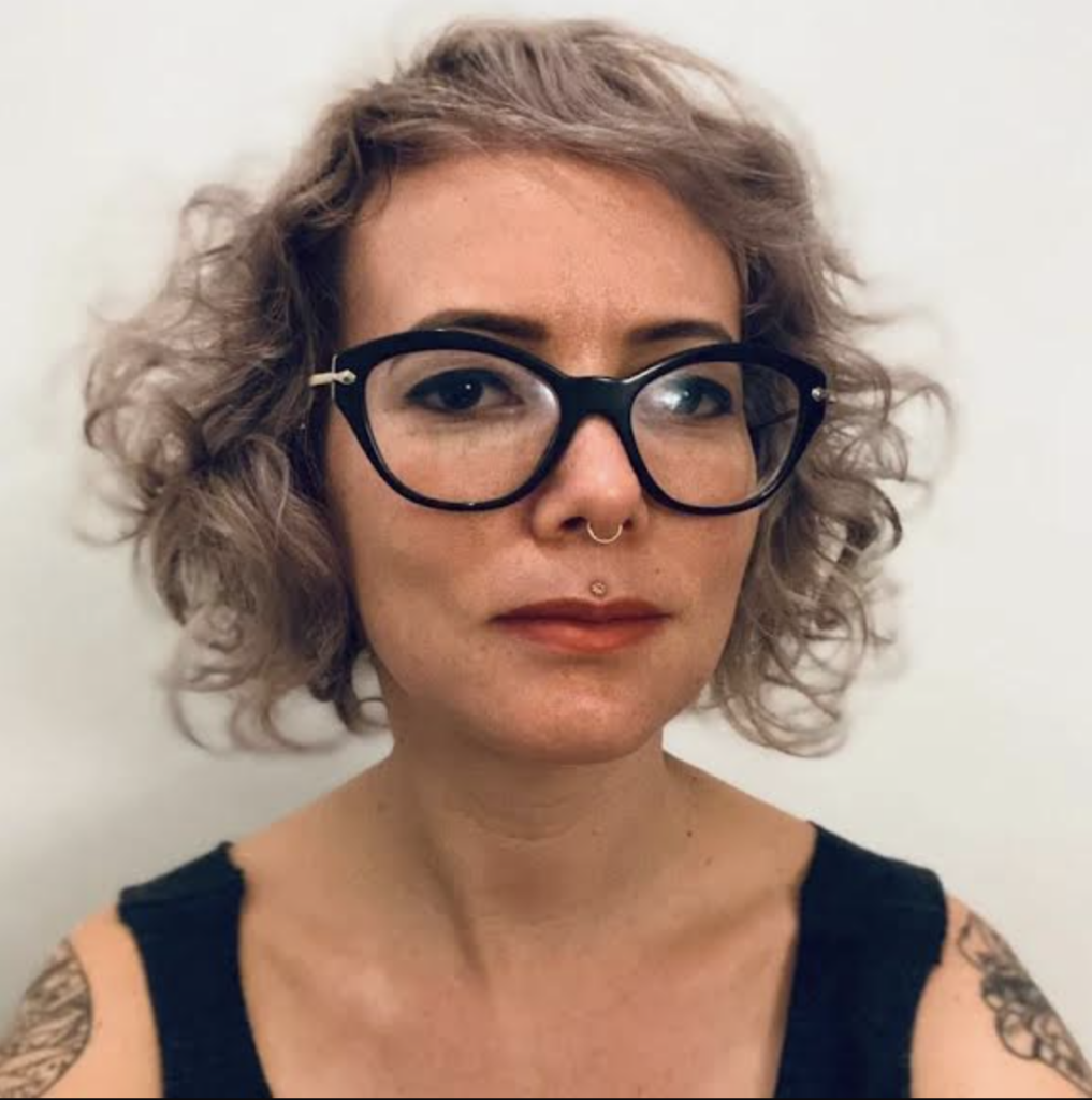 White woman with dark glasses and light brown hair wearing a black tank top against a white background