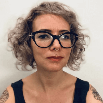 White woman with dark glasses and light brown hair wearing a black tank top against a white background