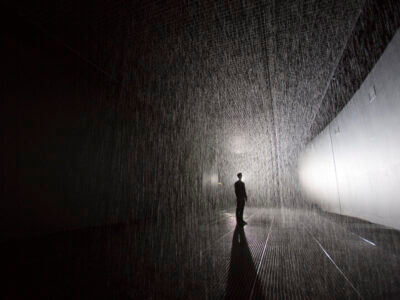 black and white image of silhouetted person standing in room with rain falling in sheets