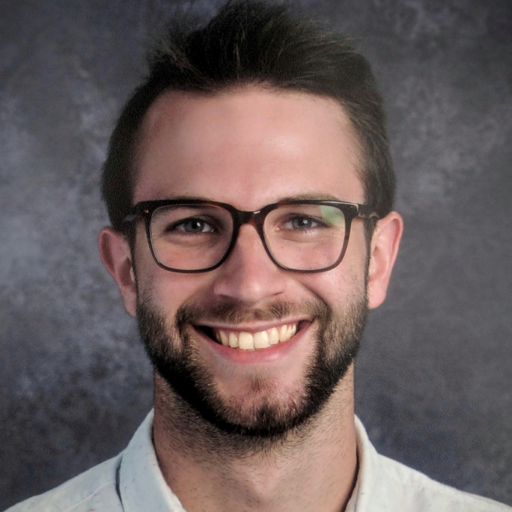 white man with brown hair and short beard with dark rimmed glasses against gray background