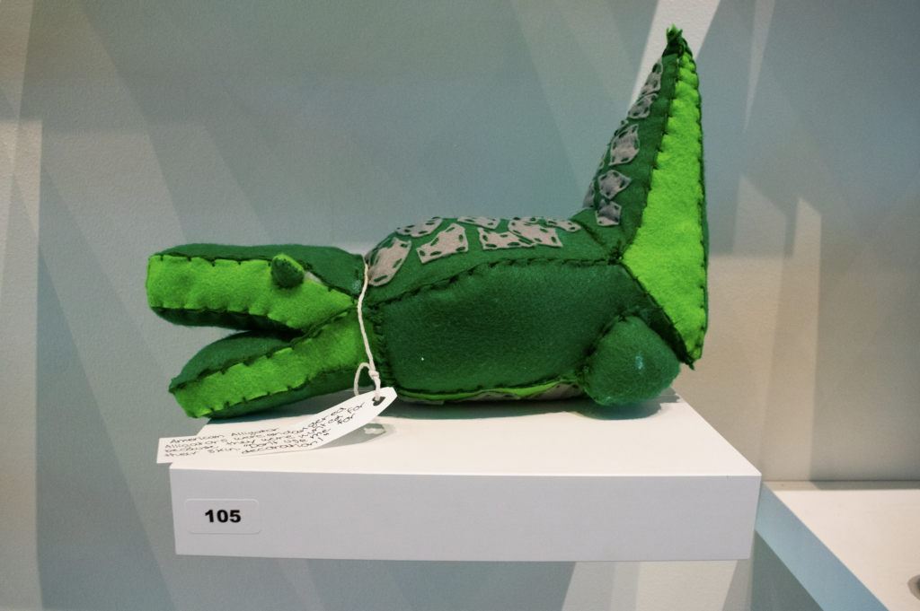 image of stuffed green alligator on white wall pedestal