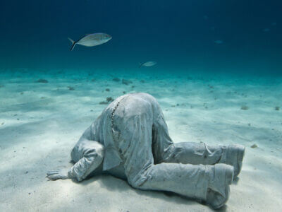 image of stone man with is head in the sand on the ocean floor