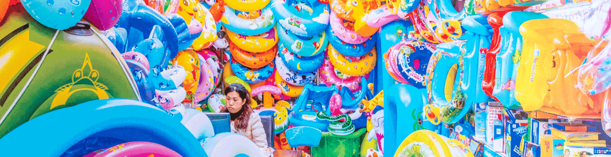multicolored plastic inflatables crowd out a young woman bored in a store